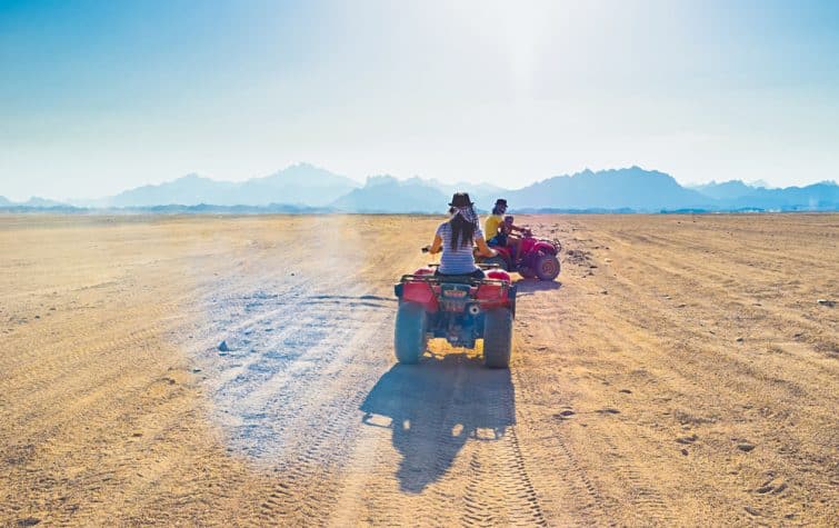 Les touristes font des quads à travers le désert du Sahara jusqu'au village bédouin, en Egypte.