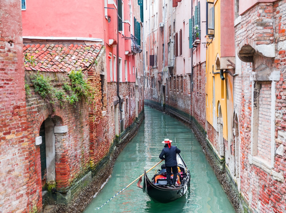 gondolier vénitien punissant la gondole à travers les eaux vertes du canal de Venise Italie