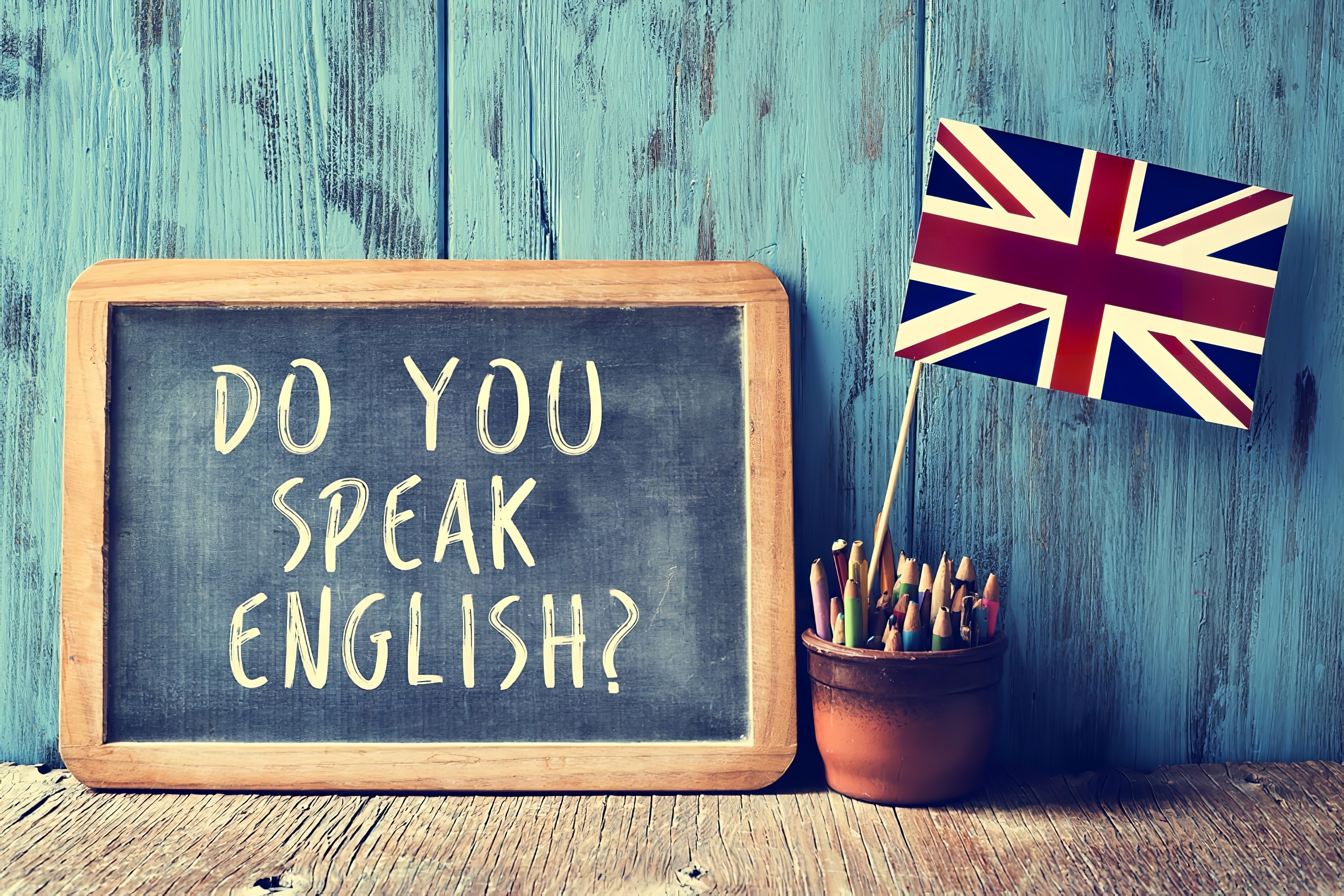 un tableau de bord avec le texte parlez-vous anglais écrit dedans, un pot avec crayons et le drapeau du Royaume-Uni, sur un bureau en bois, avec un effet filtre