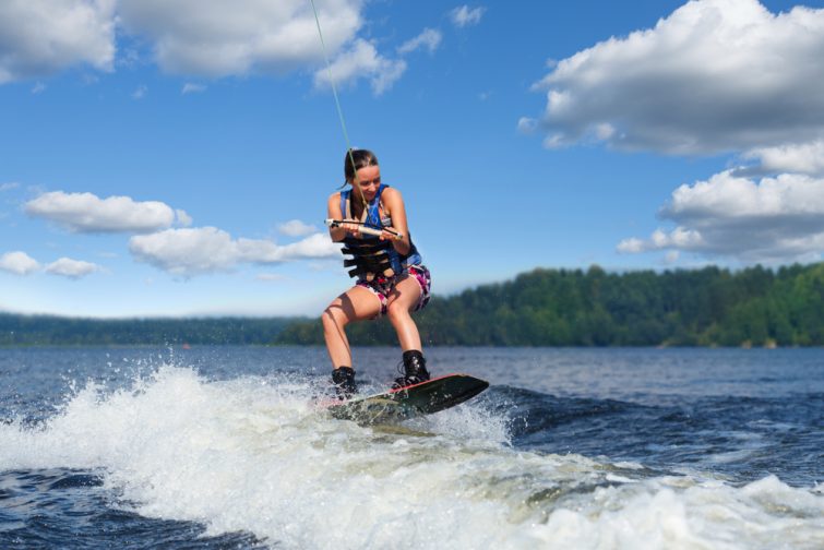 Jeune femme joliment brunette faisant du wakeboard sur une vague de bateau à moteur dans un lac d'été