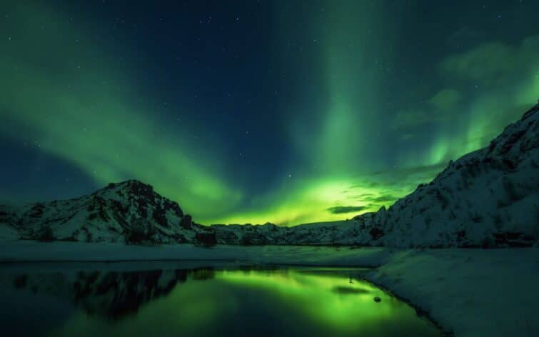 aurore boréale derrière montagne enneigée et reflet dans lac