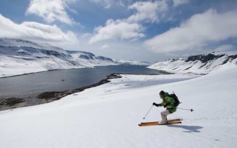 Skieur sur les pentes enneigées d'Islande, lac et soleil