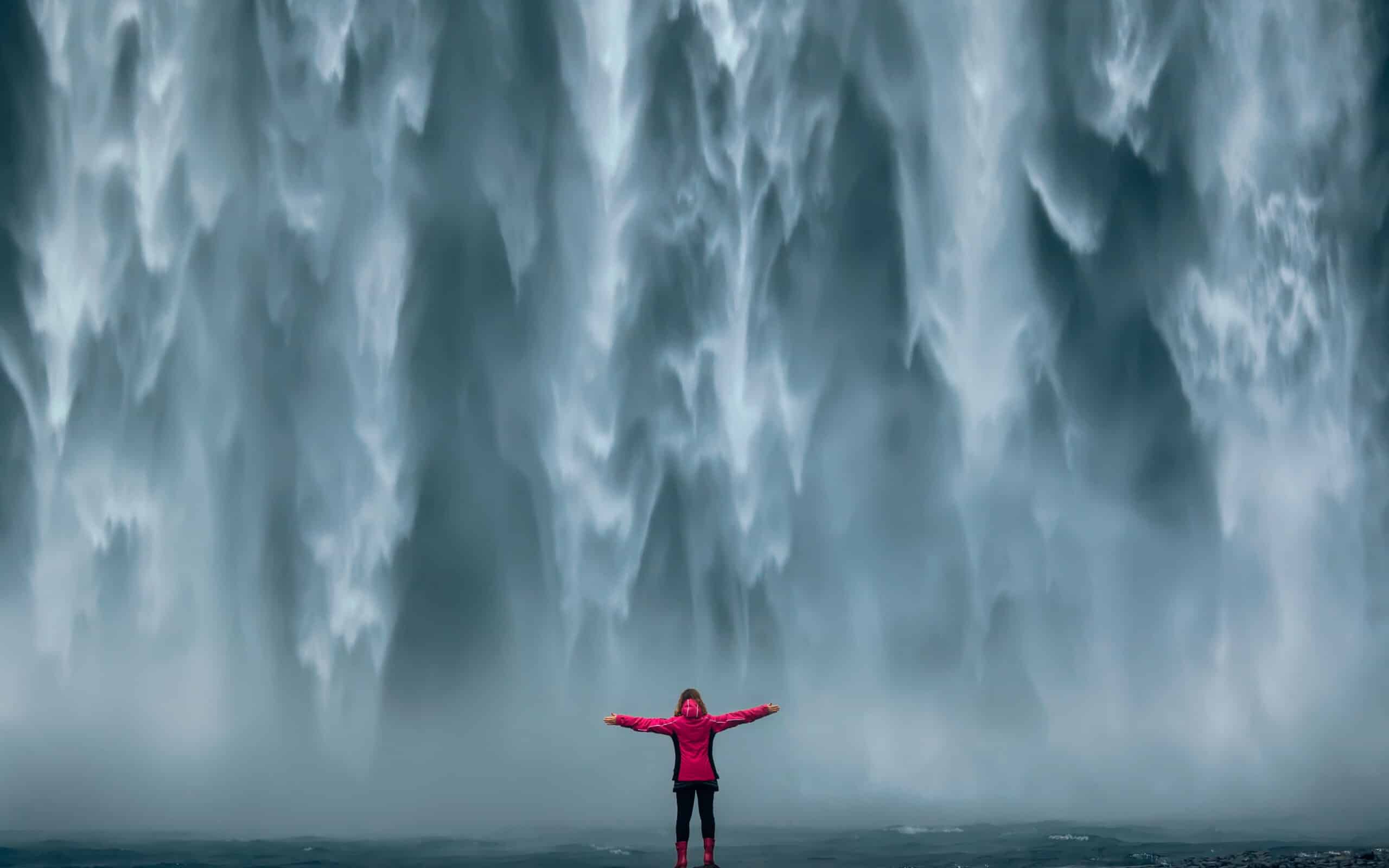 Photo de paysage islandais d'une jeune fille courageuse, fièrement debout, les bras levés devant le mur d'eau de la puissante cascade.