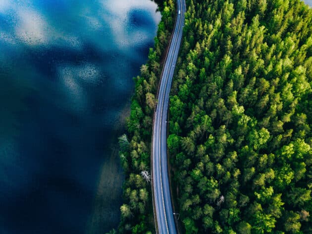 Vue aérienne d'une route traversant une forêt verte en été près d'un lac bleu en Finlande