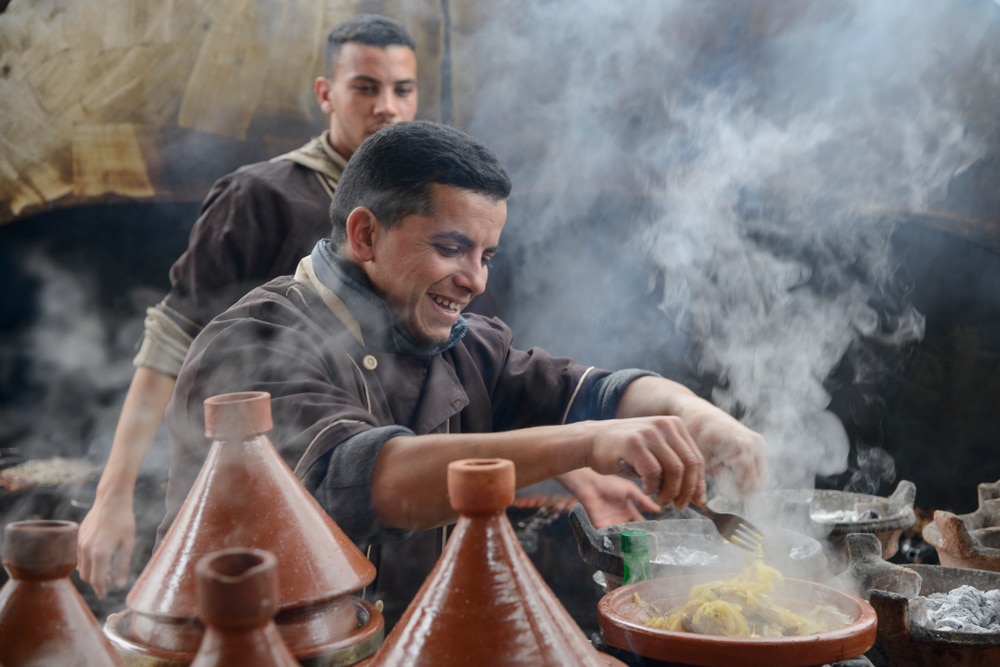 Un cuisinier prépare l'un des plats traditionnels marocains, le tajine. Il s'agit ici d'un tajine à la viande et aux oignons. On peut voir que le cuisinier prend plaisir à son travail. Place Jemaa el-Fnaa, Marrakech