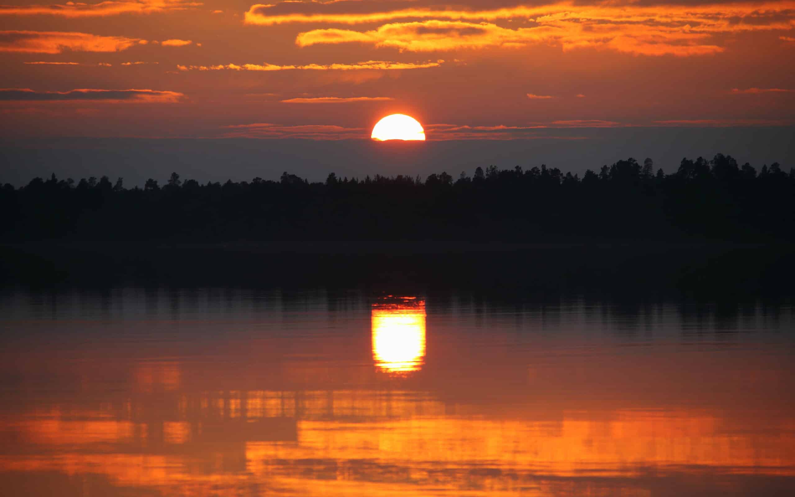 midnight sun with water reflection at lake inari in finland