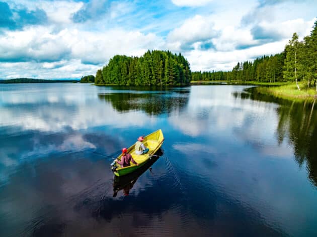 Vue aérienne d'un bateau de pêche avec une jeune femme et un homme dans un lac d'été bleu en Finlande