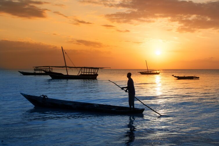 Homme sur un bateau traditionnel au large de Zanzibar au coucher du soleil