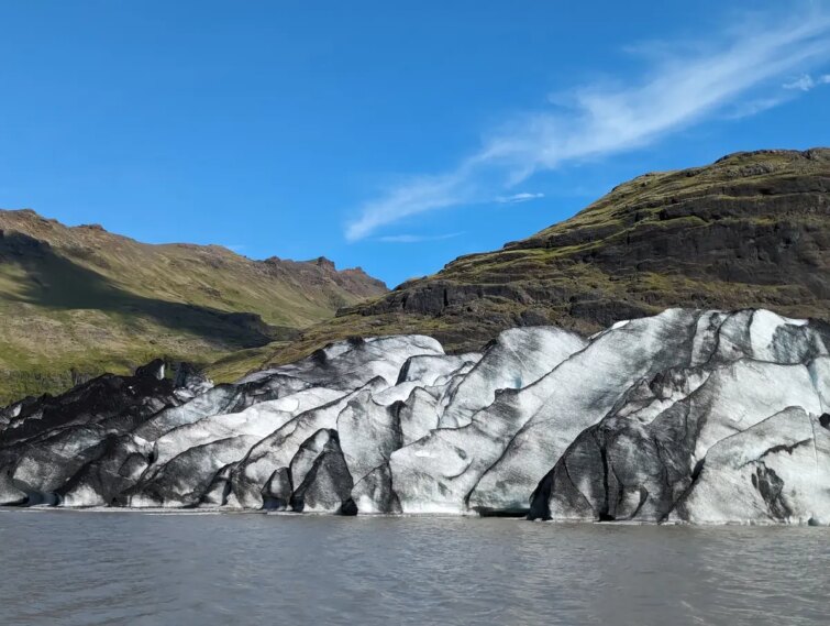 Vue panoramique du glacier Sólheimajökull en Islande, montrant des crevasses et une surface glacée avec des nuances de bleu et de gris entourée de montagnes.