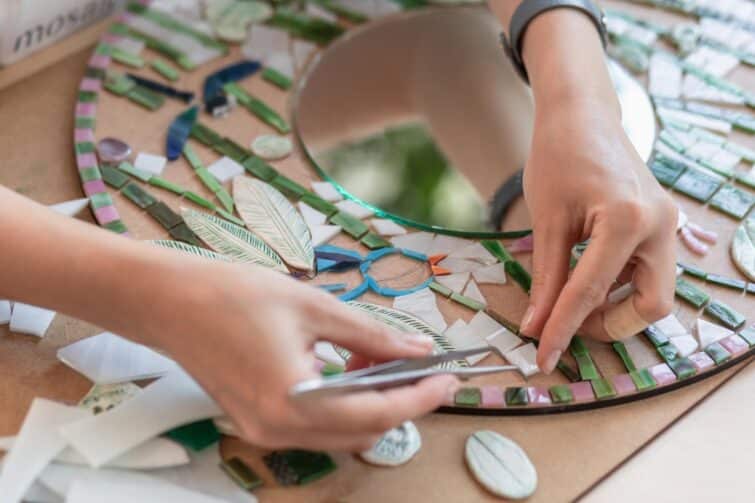 Mains de femme tenant des pinces et plaçant des carreaux de céramique pour créer une mosaïque en atelier