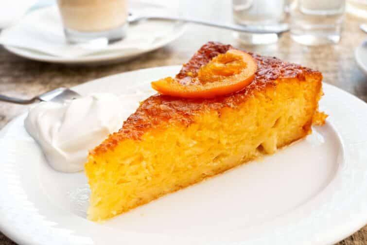 Tranche de gâteau à l'orange traditionnel grec Portokalopita avec crème sure et zeste d'orange sur plaque blanche