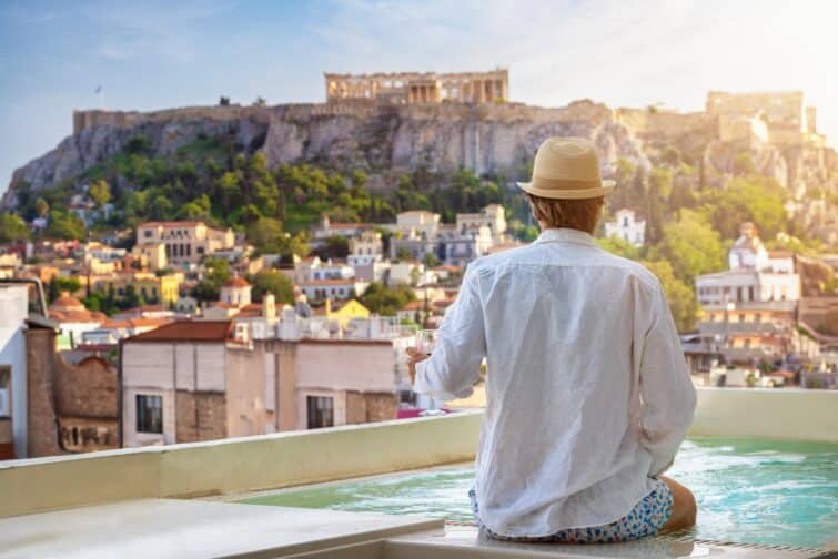 Touriste assis au bord de la piscine profitant de la vue sur l'Acropole d'Athènes