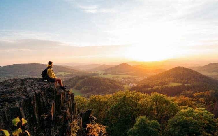 Homme confiant assis au bord d'une falaise surplombant un paysage montagneux majestueux