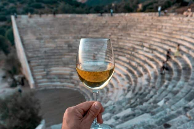 Verre de vin blanc dans une main au coucher de soleil sur fond de mer en Grèce