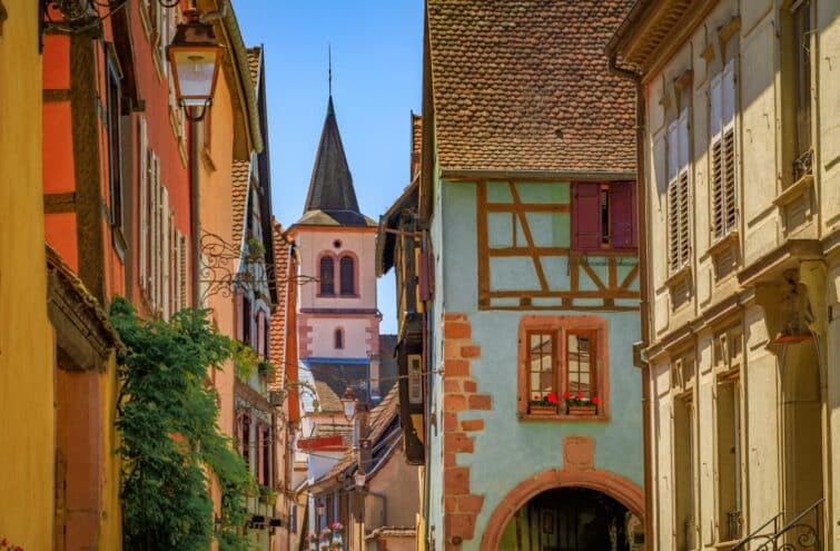 Vue sur le clocher d'une église à travers les maisons colorées traditionnelles de Riquewihr