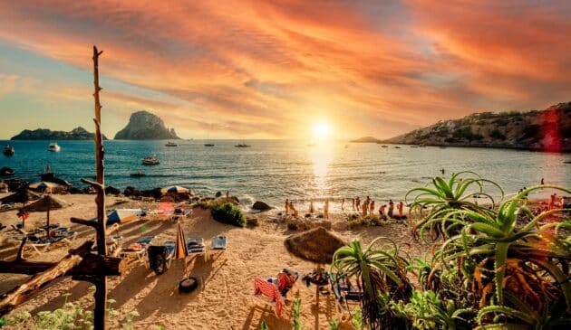 Plage de Cala d'Hort à Ibiza durant le coucher de soleil avec des gens prenant un bain de soleil