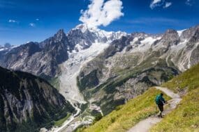 Randonneur sur le chemin du Tour du Mont Blanc en France, traversant un paysage montagneux avec vue sur des sommets enneigés
