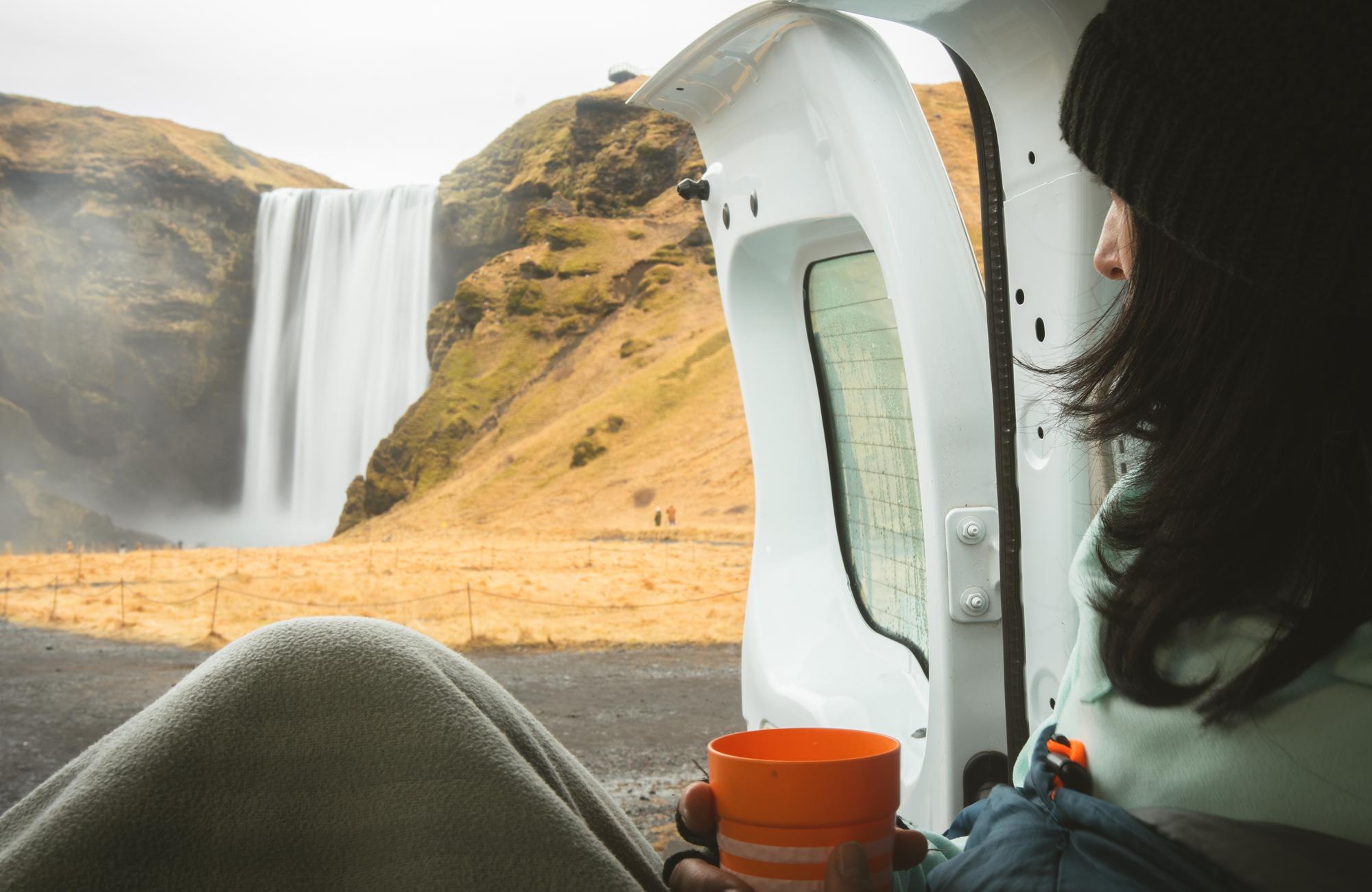 Femme dans son van aménagé observant la cascade de Skogafoss en Islande