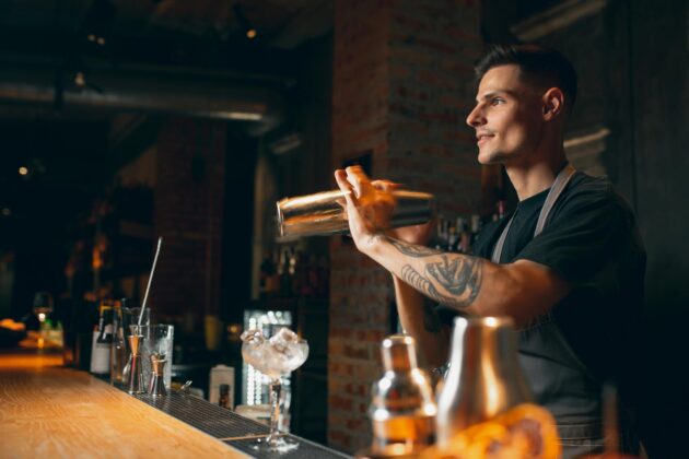 Jeune barman souriant en tablier servant un cocktail dans un bar moderne