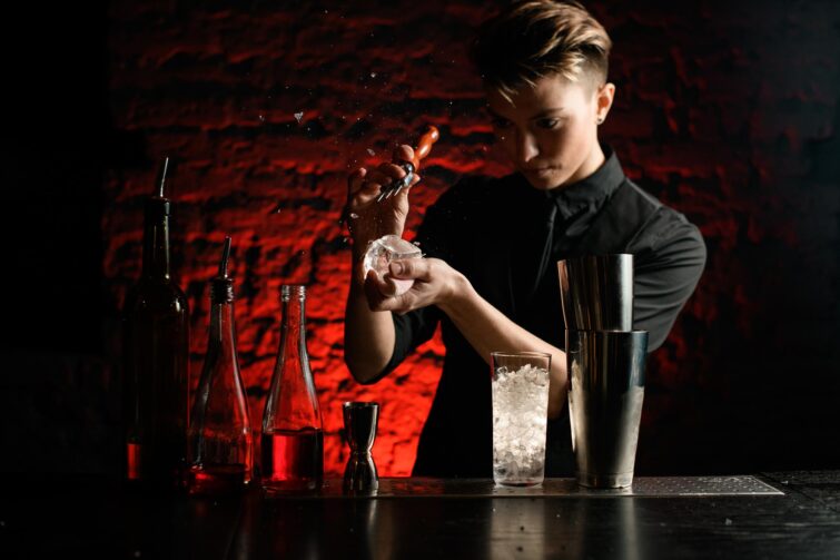 Jeune femme barmaid en vêtements noirs brisant un glaçon au bar L'Arrosoir à Toulouse, France