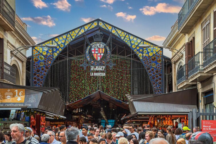 Vue animée du Mercat de la Boqueria à Barcelone, montrant divers stands de produits frais et une foule de visiteurs