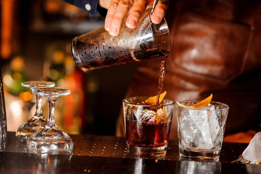 Barman qui verse de l'alcool frais dans les verres avec des glaçons sur le comptoir du bar