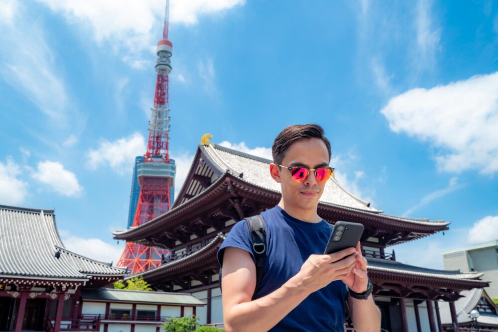 Jeune voyageur utilisant son smartphone devant l'ancien temple bouddhiste Zojo ji, près de la tour de Tokyo