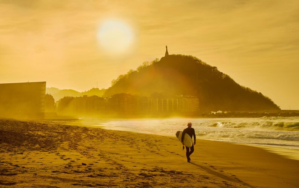 Un surfeur marchant sur la plage de Zurriola au coucher du soleil à San Sebastian