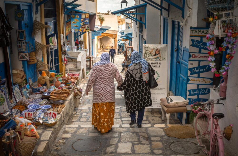 Deux Tunisiennes en foulard se promènent main dans la main devant des boutique de souvenirs dans l'ancienne médina de Sousse
